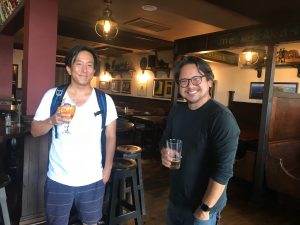 Two men standing in a pub smiling at camera holding a drink